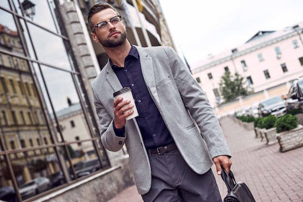 Genießen Sie seine Kaffeepause, ein hübscher junger Mann, der beim Gehen Einwegbecher und Aktentasche hält