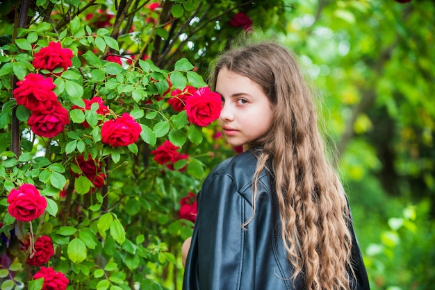 Genießt ihren Tag. frühlingsblühender Baum. Sommer Natur. weibliche friseurmode. kleines Mädchen mit lockigem Haar. kleine Schönheit im weißen Kleid. Kind trägt Lederjacke. Kind genießen Rosenblüte im Park.