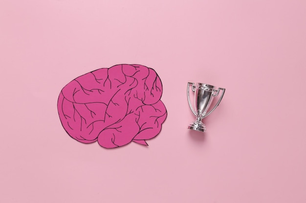 Gênio intelectual cérebro cortado em papel com taça de vencedor em fundo rosa