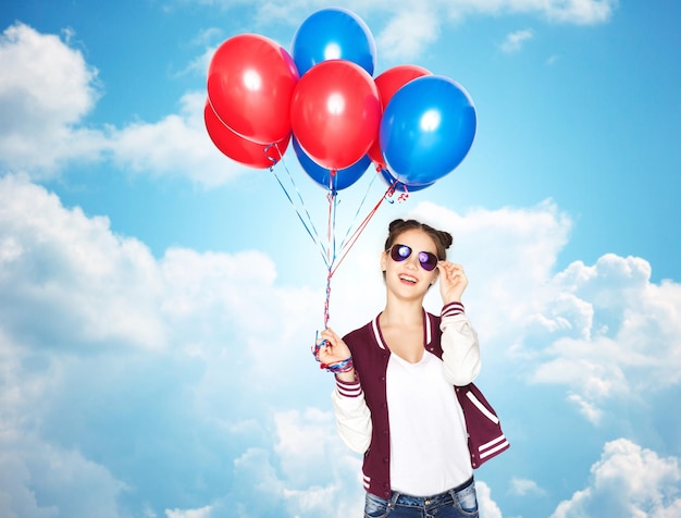 gente, adolescentes, vacaciones, fiesta y concepto de verano - feliz y sonriente adolescente con gafas de sol con globos de helio sobre el cielo azul y el fondo de las nubes