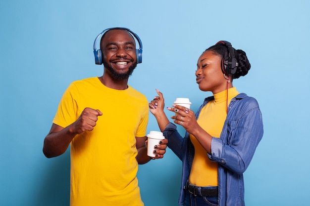 Gente alegre bailando y escuchando música con auriculares, haciendo divertidos movimientos de baile en cámara. Hombre y mujer románticos divirtiéndose con la canción mp3 en los auriculares. Pareja con audio riendo.