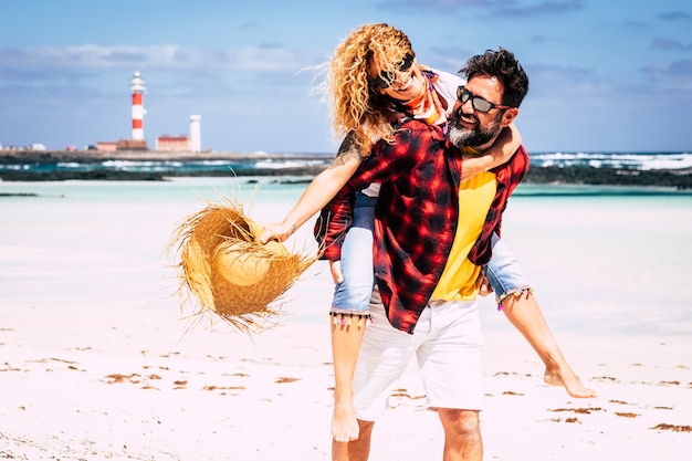 Foto gente alegre feliz pareja alegre jugando juntos en el amor con el hombre que lleva a la mujer riendo mucho divirtiéndose en la playa en un día soleado de vacaciones de verano