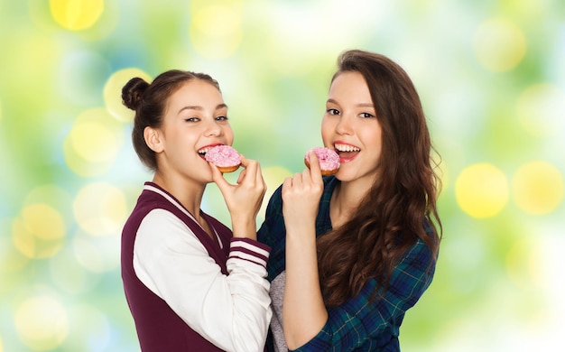 gente, amigos, adolescentes y el concepto de amistad - felices y sonrientes adolescentes bonitas con donuts comiendo y divirtiéndose durante las vacaciones verdes luces de fondo