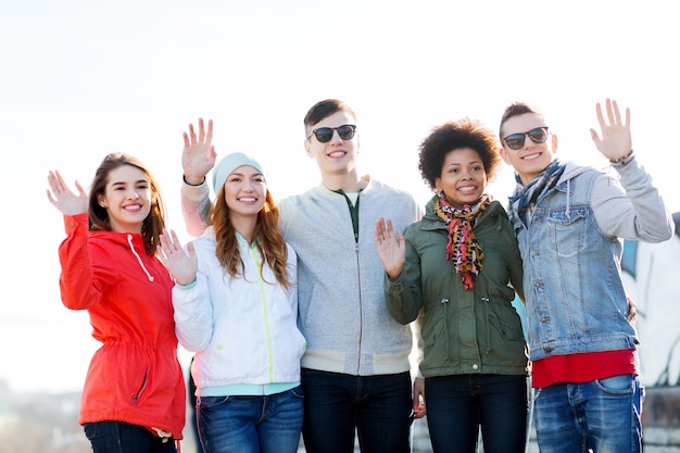 gente, amistad y concepto internacional - grupo de amigos adolescentes felices agitando las manos en la calle de la ciudad