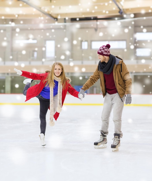 Foto gente, amistad, deporte y concepto de ocio - pareja feliz tomándose de la mano en la pista de patinaje