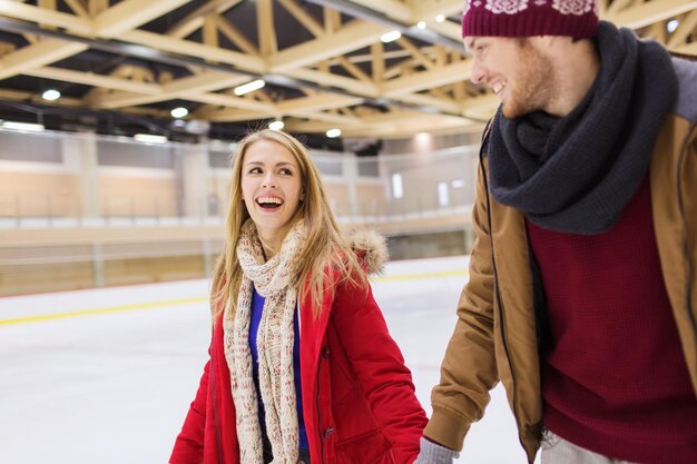 gente, amistad, deporte y concepto de ocio - pareja feliz tomándose de la mano en la pista de patinaje