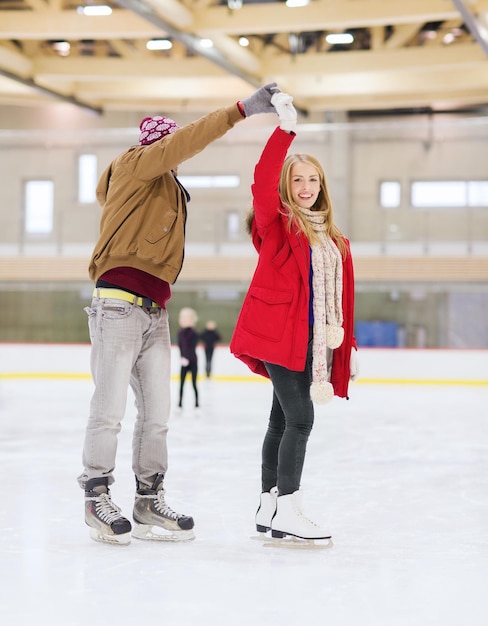 gente, amistad, deporte y concepto de ocio - pareja feliz tomándose de la mano en la pista de patinaje