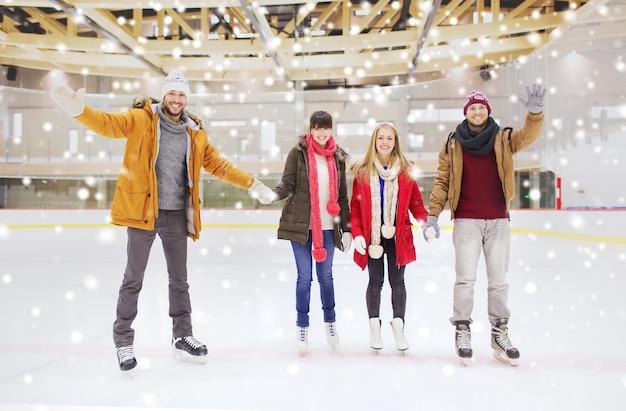 gente, amistad, gesto, deporte y concepto de ocio - amigos felices saludando con la mano en la pista de patinaje