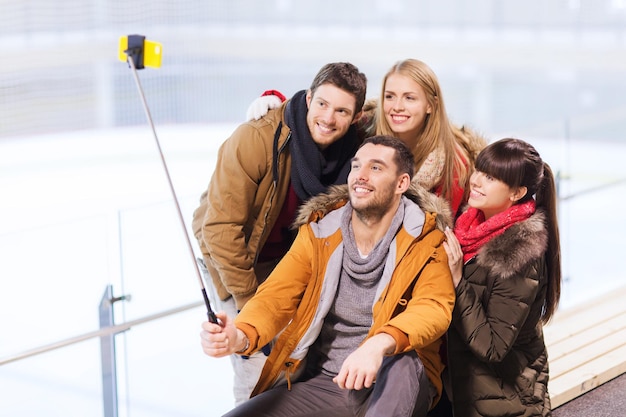 gente, amistad, tecnología y concepto de ocio - amigos felices tomando fotos con un selfie de smartphone en una pista de patinaje