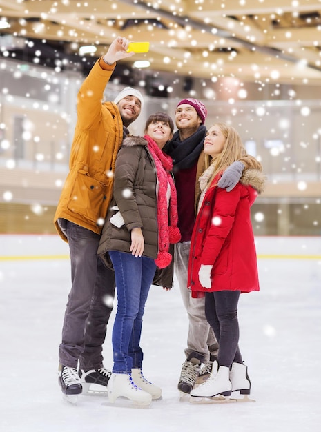 gente, amistad, tecnología y concepto de ocio - amigos felices tomándose selfie con un smartphone en una pista de patinaje