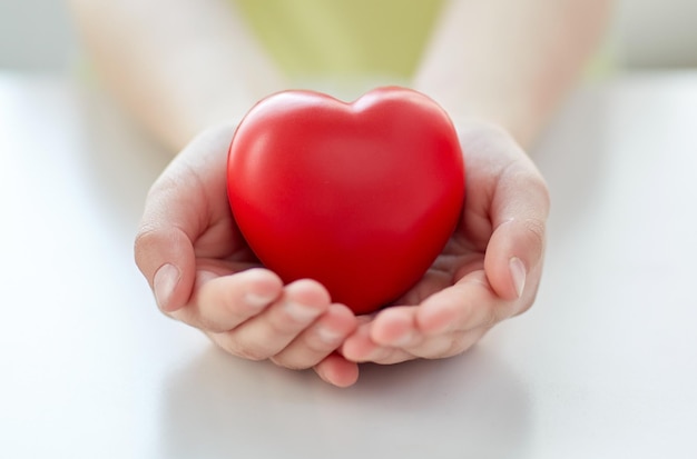 gente, amor, caridad y concepto familiar - cierre de las manos de los niños con forma de corazón rojo en casa