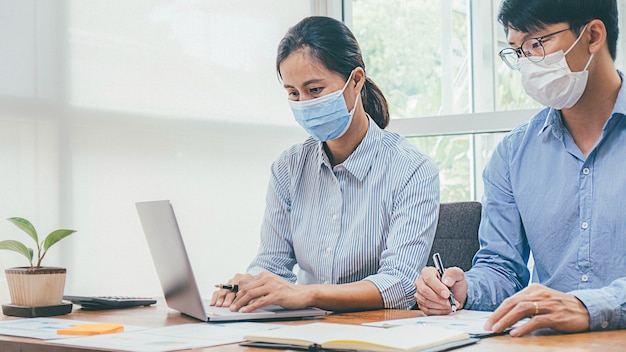 Gente asiática de negocios exitoso trabajo en equipo con máscara médica y trabajo. Trabajo desde oficinas privadas Distanciamiento social entre situación de brote de coronavirus