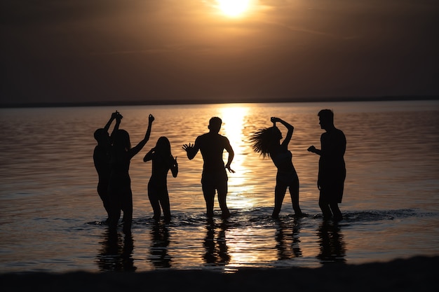 La gente bailando en la fiesta nocturna en la playa contra la puesta de sol.