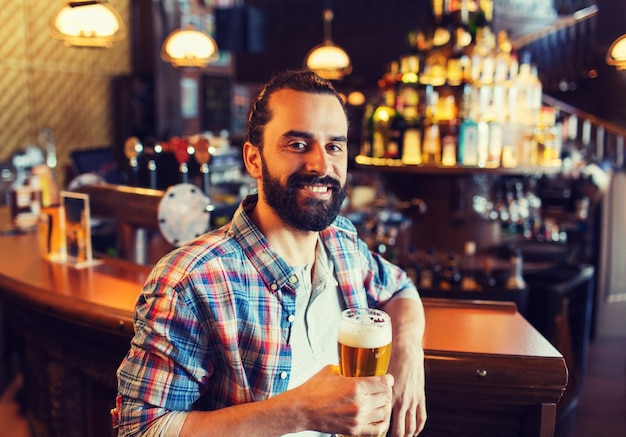 gente, bebidas, alcohol y concepto de ocio - joven feliz bebiendo cerveza en el bar o pub