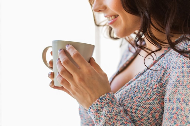 gente, bebidas y concepto de ocio - cerca de una joven feliz con una taza de té o café en casa