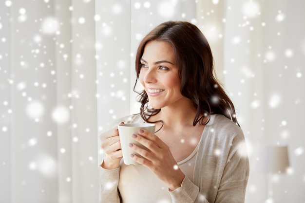 gente, bebidas, invierno y concepto de navidad - mujer joven feliz con una taza de té o café en casa sobre la nieve