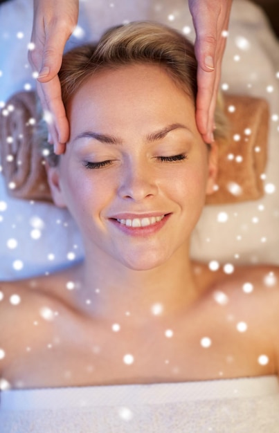 gente, belleza, spa, invierno y concepto de relajación - cerca de una hermosa joven acostada con los ojos cerrados y con masaje facial o de cabeza en el spa con efecto de nieve