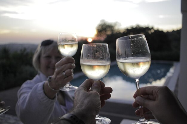 Foto gente brindando vino contra el cielo durante la puesta de sol