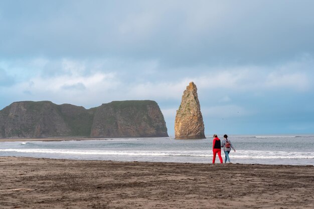 La gente camina a lo largo de la orilla del océano en la isla de Kunashir con vistas a los acantilados costeros