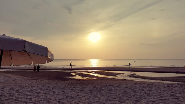 Gente caminando por la playa mientras la hora del amanecer.