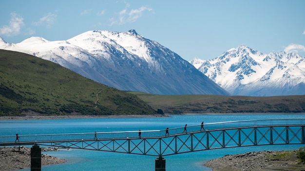 Gente caminando por el puente sobre el lago turquesa con montañas nevadas tekaponew zelanda