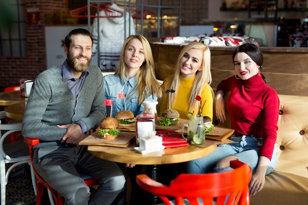 La gente cena juntos en una mesa en un café. Amigos felices comen hamburguesas y beben cócteles en el restaurante