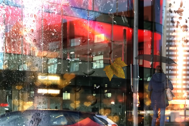 Foto gente de la ciudad lluviosa con sombrillas hojas amarillas reflejo de luz nocturna en la ventana