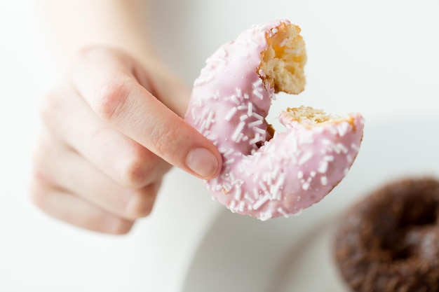 gente, comida, comida chatarra y concepto de alimentación - cierre de la mano femenina sosteniendo un donut glaseado mordido