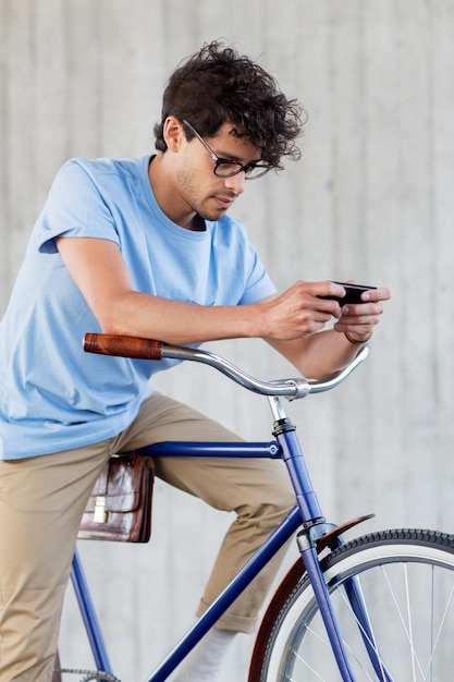 gente, comunicación, tecnología, ocio y estilo de vida - hombre hipster enviando mensajes de texto en un teléfono inteligente con bicicleta fija en la calle de la ciudad