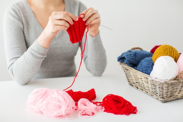 gente y concepto de costura - manos de mujer tejiendo con agujas e hilo rojo