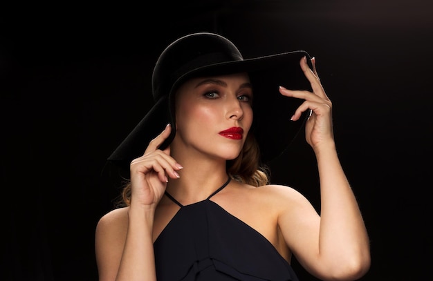 gente, concepto de lujo y moda - hermosa mujer con sombrero negro sobre fondo oscuro