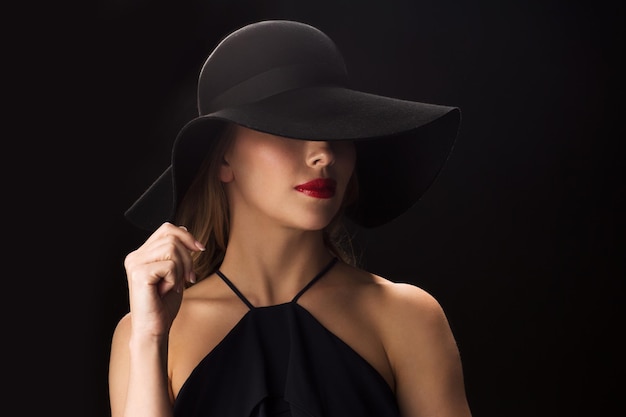 gente, concepto de lujo y moda - hermosa mujer con sombrero negro sobre fondo oscuro