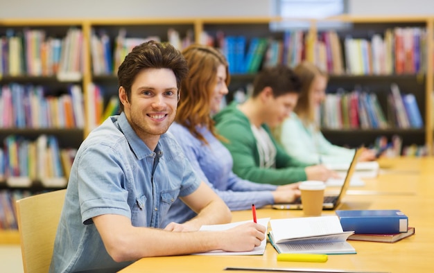 gente, conocimiento, educación y concepto escolar - estudiante feliz con libros escribiendo en un cuaderno en la biblioteca