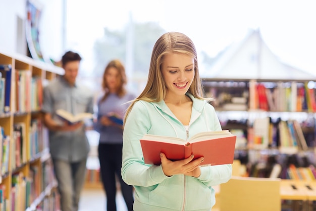 gente, conocimiento, educación y concepto escolar - estudiante feliz o mujer joven con un libro en la biblioteca