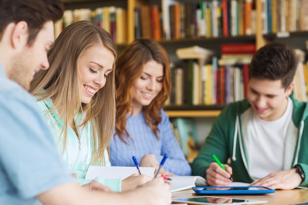 gente, conocimiento, educación y concepto escolar - grupo de estudiantes felices escribiendo en cuadernos en la biblioteca