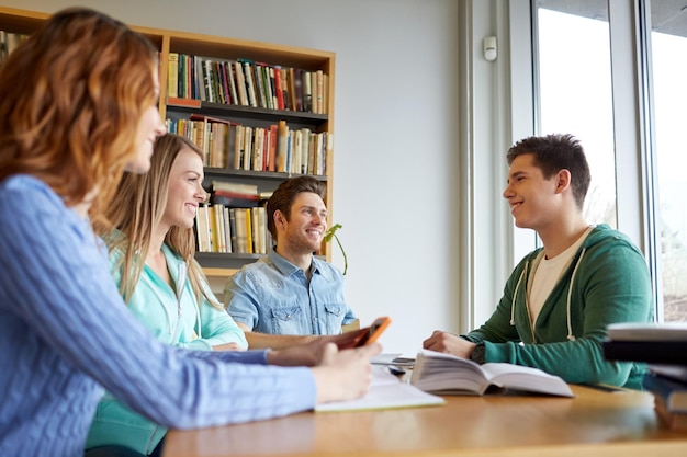 gente, conocimiento, educación y concepto escolar - grupo de estudiantes felices leyendo libros y preparándose para el examen en la biblioteca