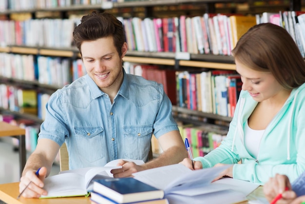 gente, conocimiento, educación y concepto escolar - grupo de estudiantes felices con libros preparándose para el examen en la biblioteca