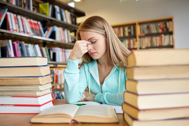 gente, conocimiento, educación, literatura y concepto escolar - estudiante aburrida o mujer joven con libros soñando en la biblioteca