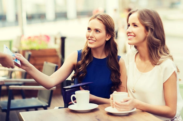 gente, consumismo, estilo de vida y concepto de amistad - mujeres jóvenes sonrientes que dan dinero a la camarera y pagan por un café en un café al aire libre