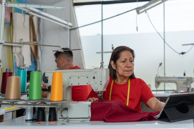 Gente cosiendo en un taller usando máquinas y una tableta digital