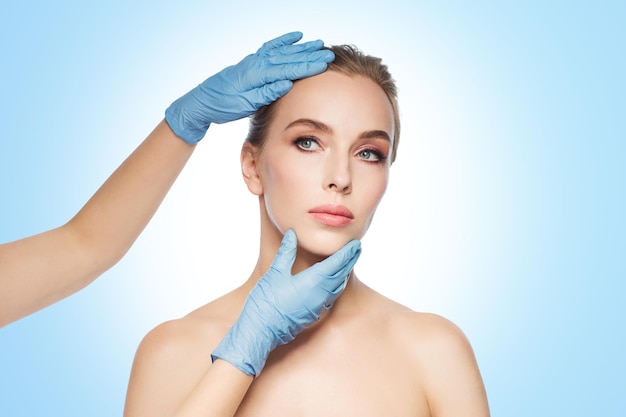 gente, cosmetología, cirugía plástica y concepto de belleza - manos de cirujano o esteticista tocando la cara de la mujer sobre fondo azul