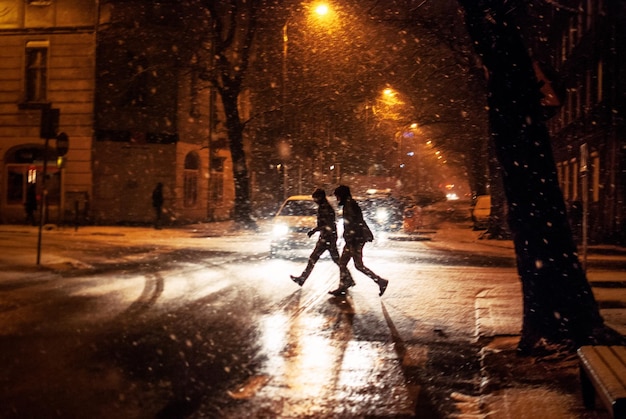 Gente cruzando la carretera durante la nieve en la ciudad por la noche