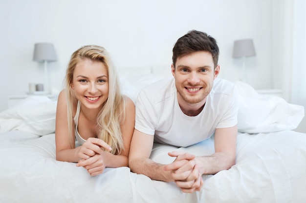 gente, descanso, amor, relaciones y concepto de felicidad - pareja feliz acostada en la cama en casa