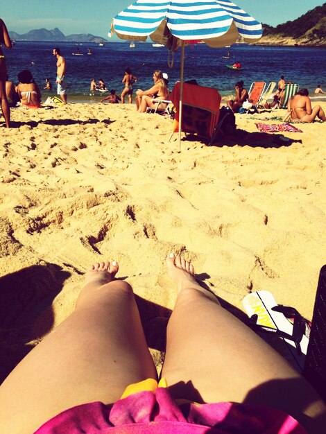 Foto la gente disfrutando en la playa con la sección baja de la mujer seductora en primer plano