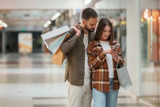 Foto gente emocionada con un teléfono inteligente una pareja joven está en el supermercado juntos