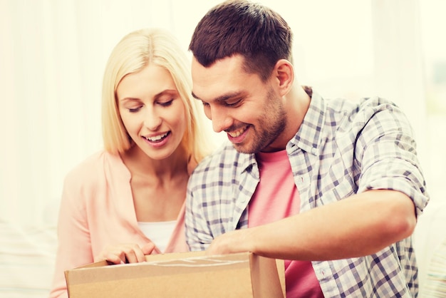 gente, entrega, envío y concepto de servicio postal - pareja feliz abriendo caja de cartón o paquete en casa