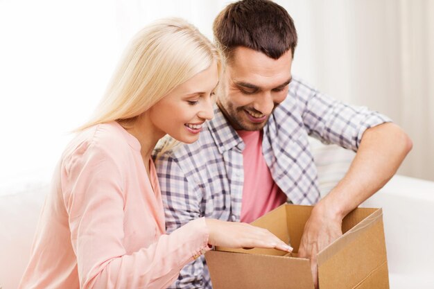 gente, entrega, envío y concepto de servicio postal - pareja feliz abriendo caja de cartón o paquete en casa