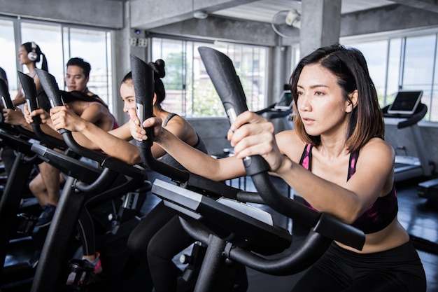 La gente está haciendo ejercicio con cardio en la clase de spinning con una máquina de ejercicios en el gimnasio.