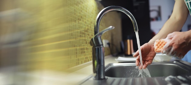 La gente está lavando los platos Solución de limpieza Una botella blanca con esponjas de gel para lavar platos y guantes de goma en el fondo de un fregadero con platos sucios