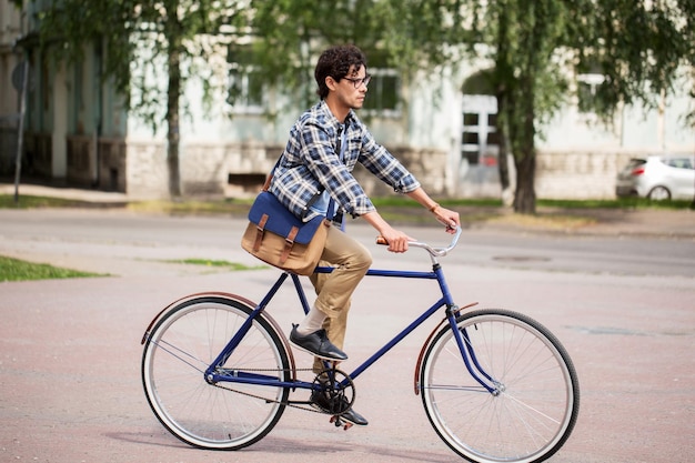 gente, estilo, ocio y estilo de vida - joven hipster con bandolera montando bicicleta fija en la calle de la ciudad de tallin